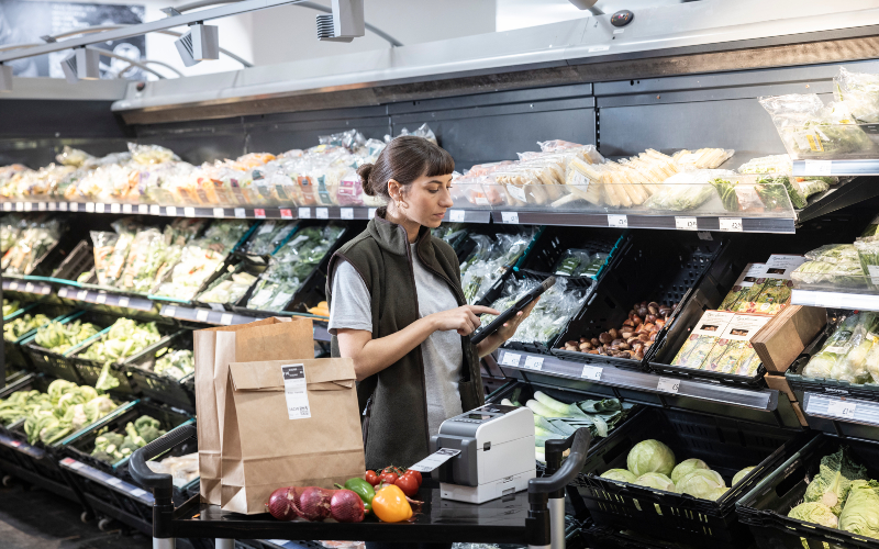 Woman in the supermarket holding a clipboard surrounded by vegetables